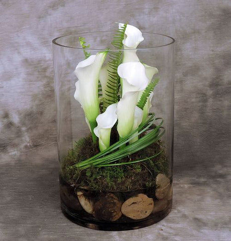 Large glass cylinder filled with white calla lilies, moss and river rock