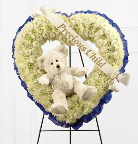 Precious child standing heart funeral piece of all white flowers with white teddy bear