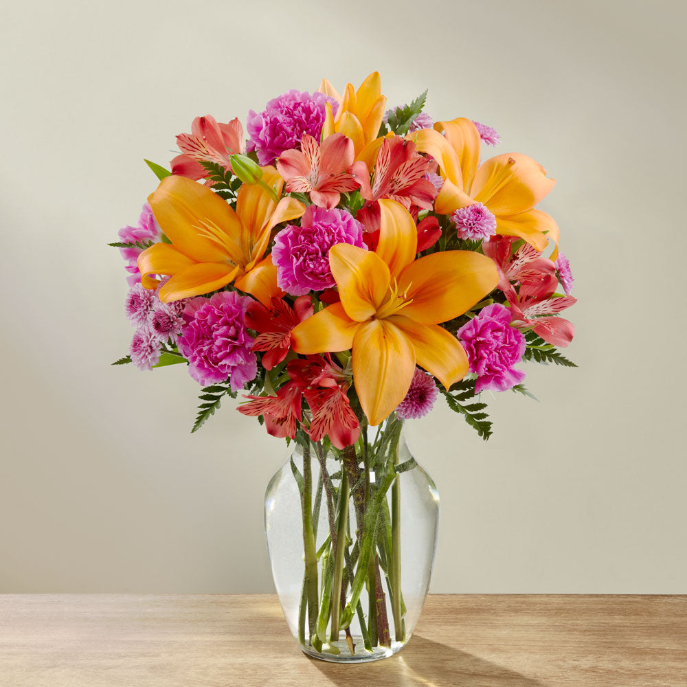 Orange lilies and hot pink mini carns in a glass vase Deluxe