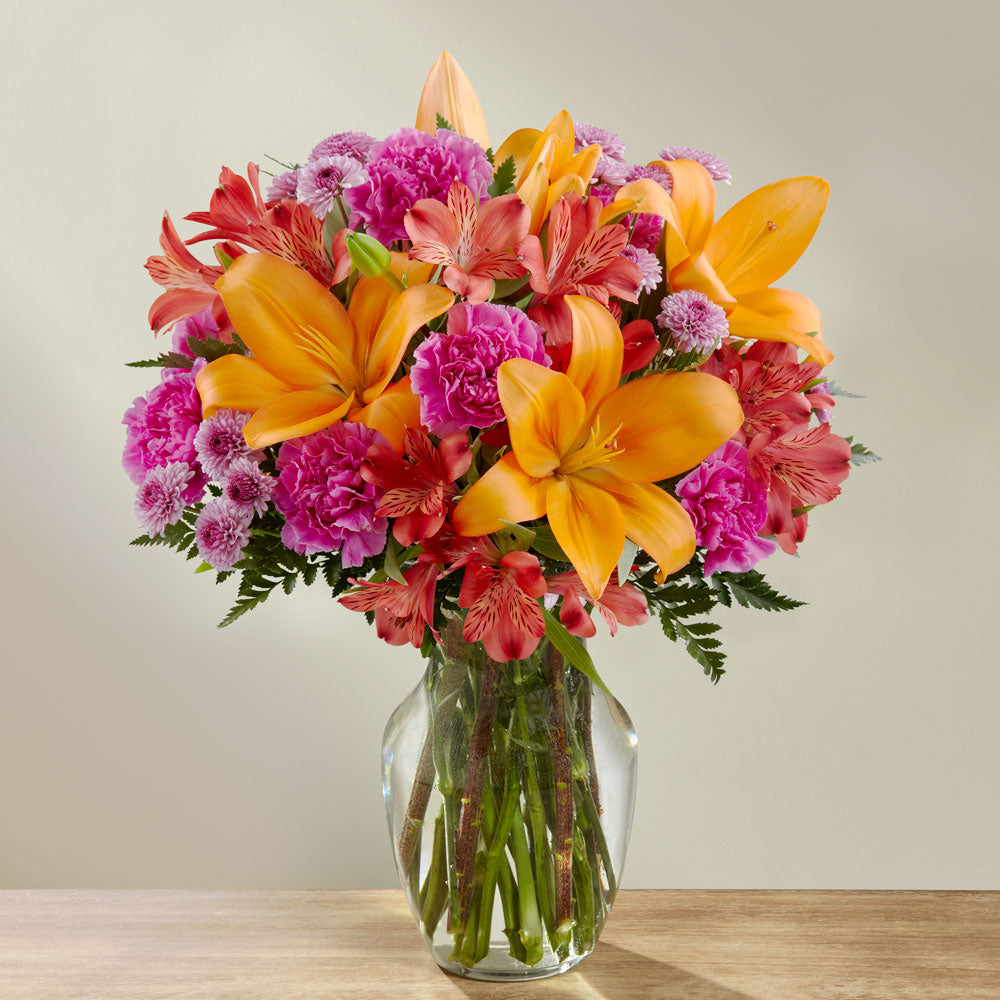 Orange lilies and hot pink mini carns in a glass vase Premium